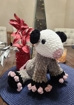 Crocheted plush opossum sitting on a blue textured surface with decorative elements in the background.