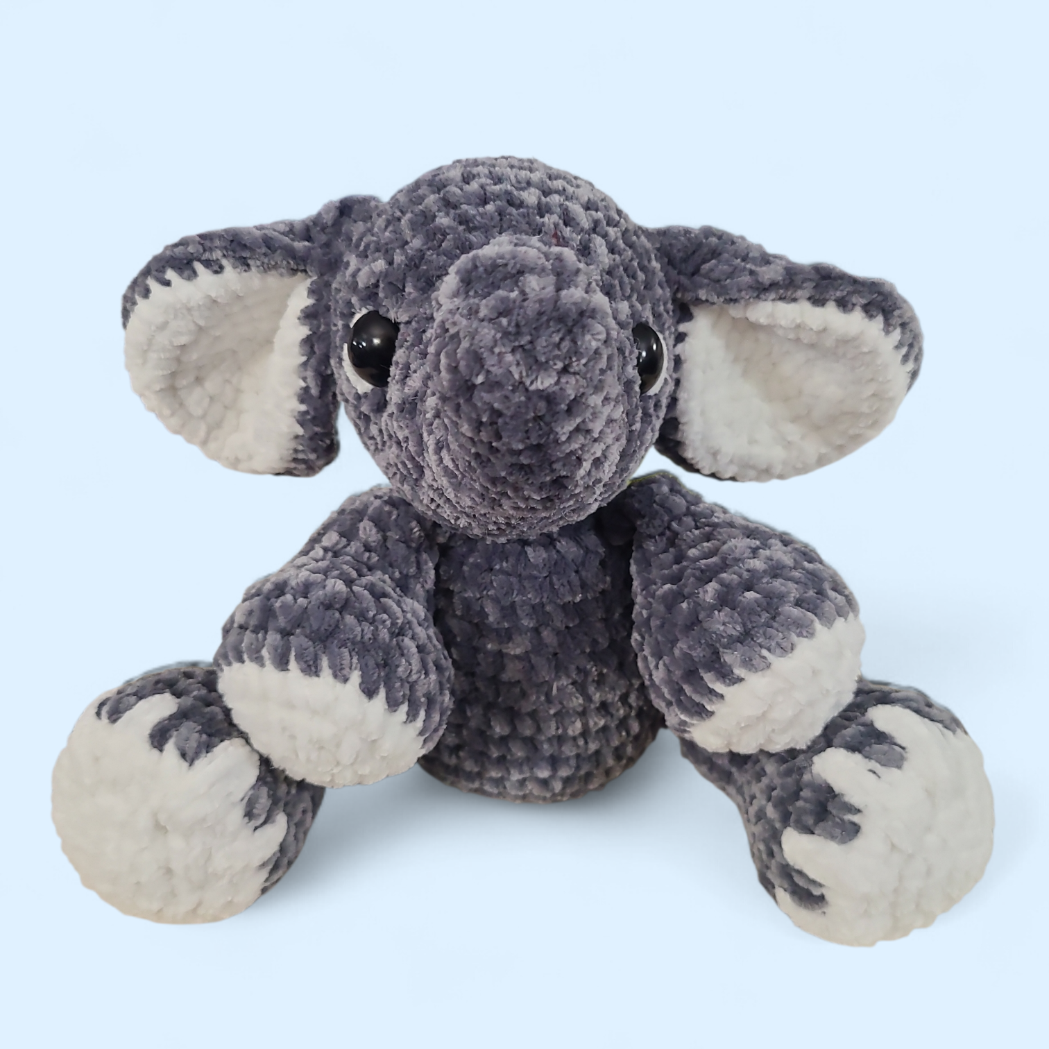 Crocheted grey seated elephant on a light blue background