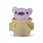 Crocheted yellow and pink variegated bear with a pink nose and wearing a yellow hoodie on a white background