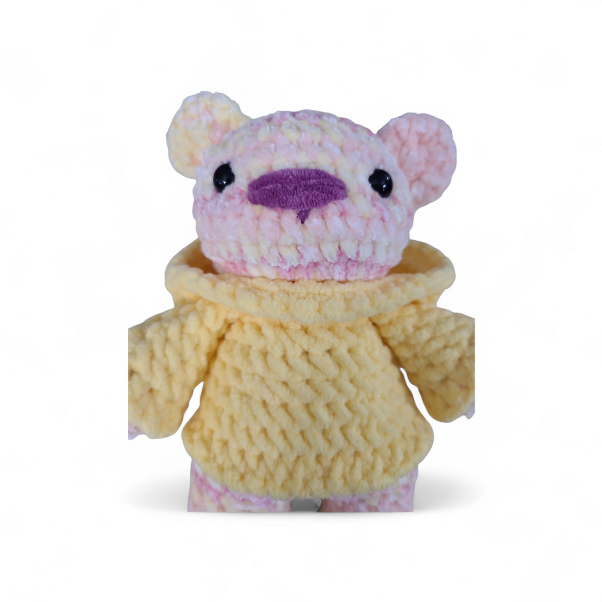 Crocheted yellow and pink variegated bear with a pink nose and wearing a yellow hoodie on a white background