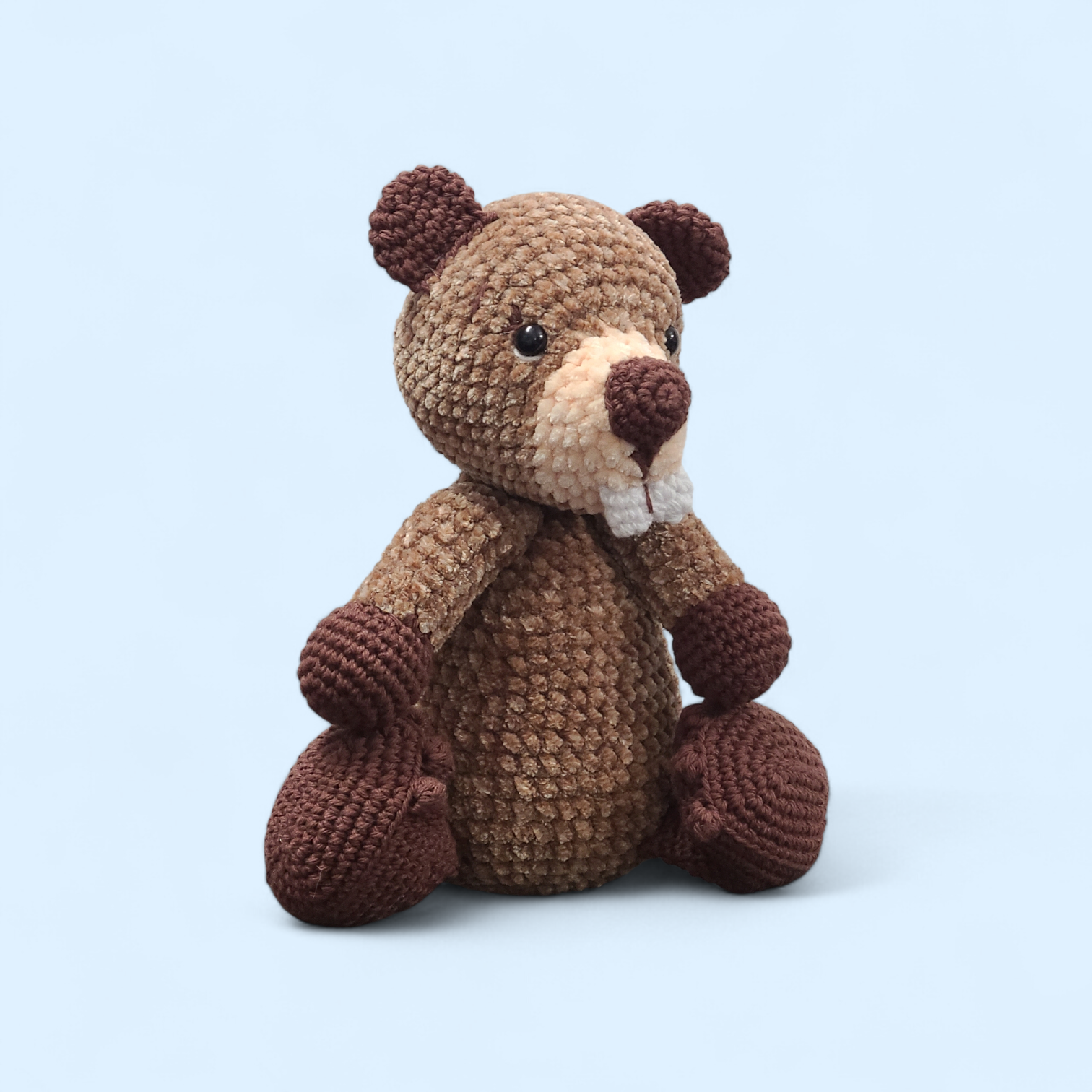 Crocheted beaver with buck teeth and brown body on a light blue background