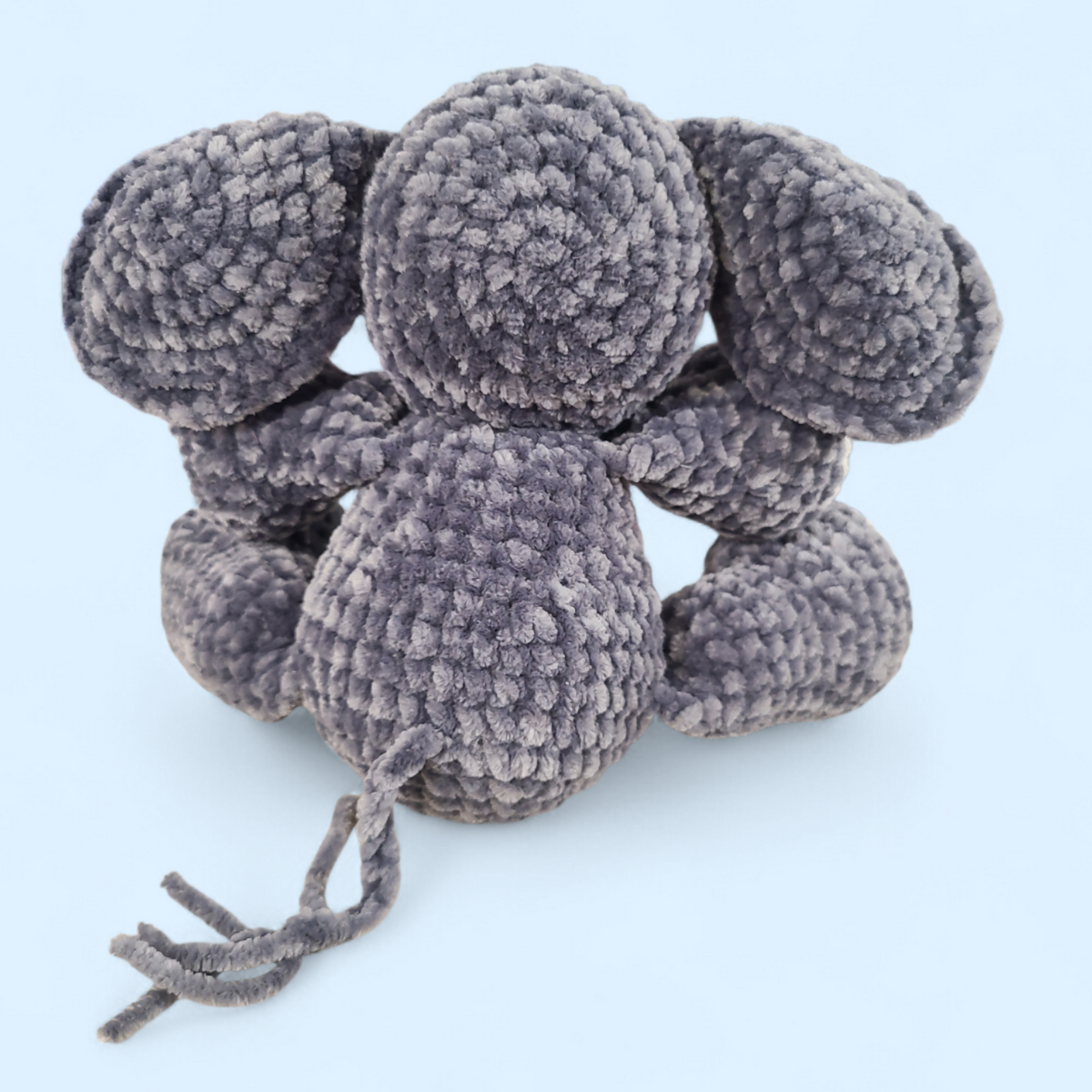 Crocheted grey seated elephant on a light blue background