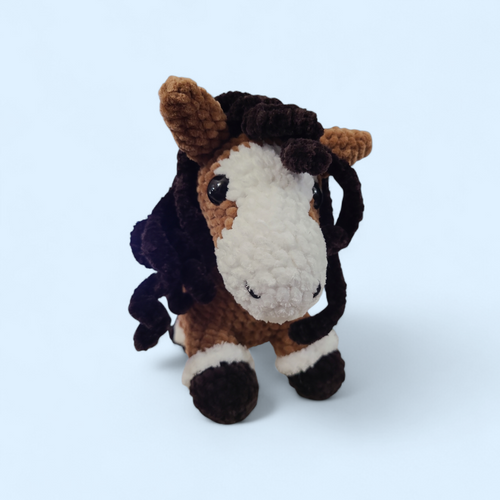 Crocheted horse toy with a white face and brown body on a light blue background