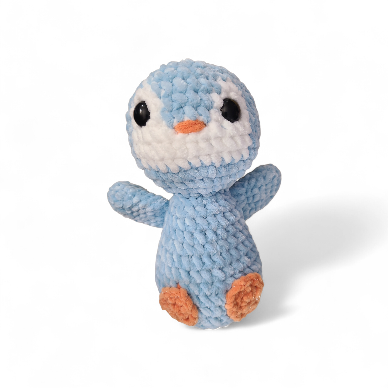 Crochet baby penguin with blue body and orange beak on a white background
