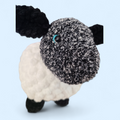 Crocheted sheep with black face and white body on a light blue background