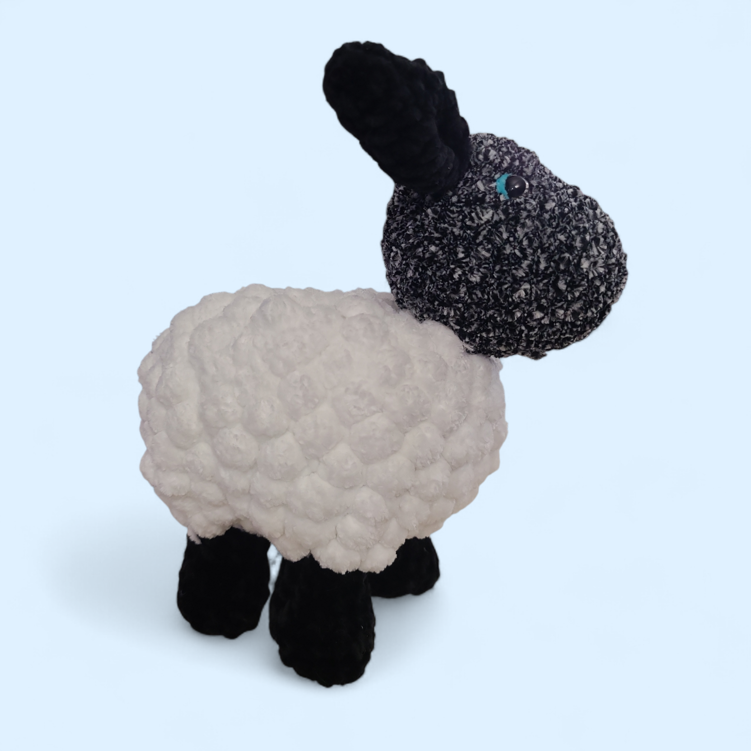 Crocheted sheep with a black face on a light blue background
