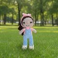 Crocheted doll with pink hair tie and blue overalls on a white background