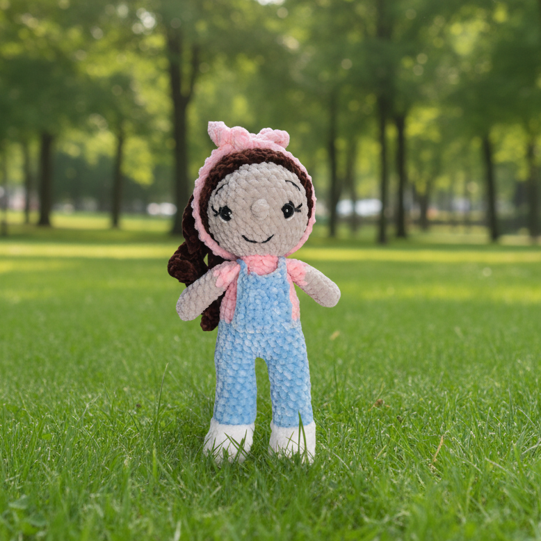 Crocheted doll with pink hair tie and blue overalls on a white background