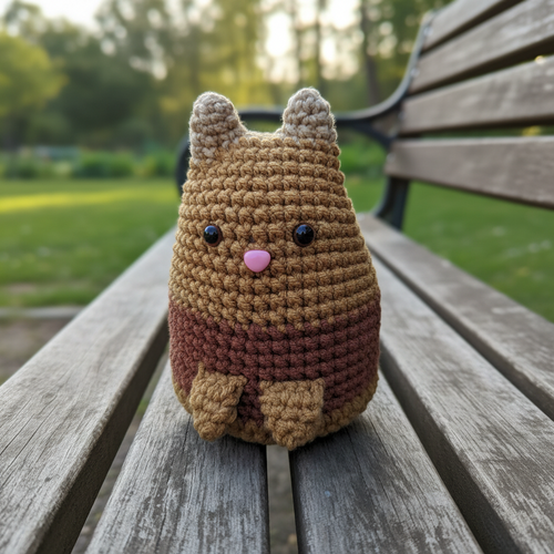 Crocheted Dumpling cat plushie with a gradient brown color scheme on a light green background